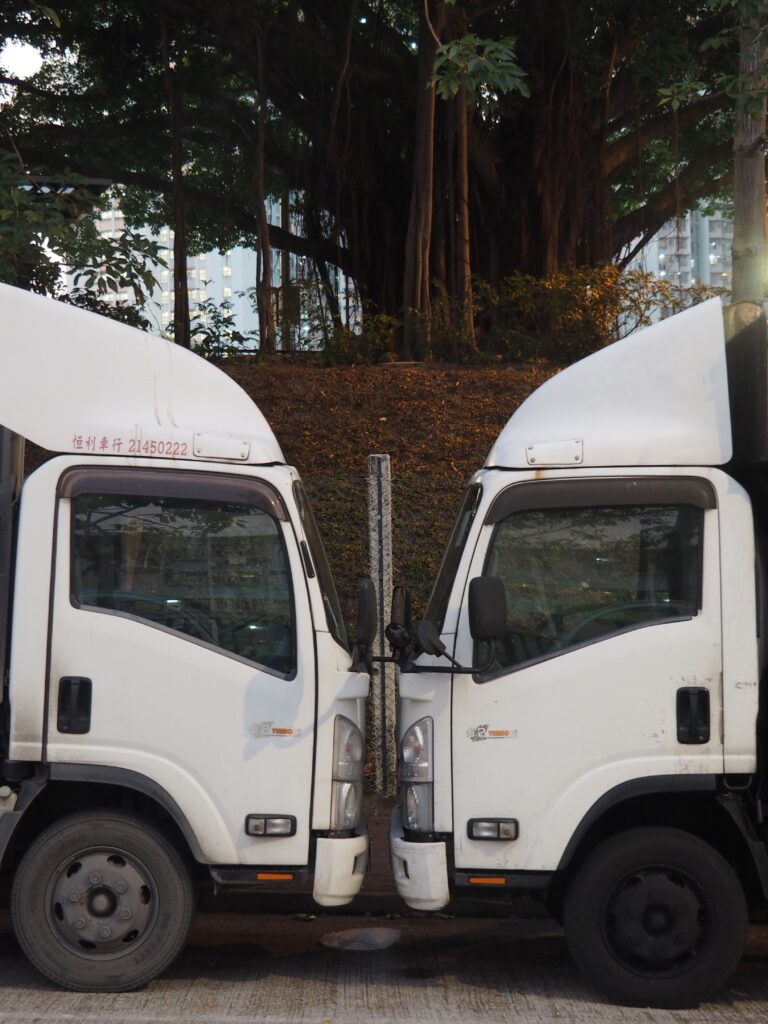 Two symmetrical white trucks parked opposite each other in a Hong Kong street, creating a mirrored urban scene.